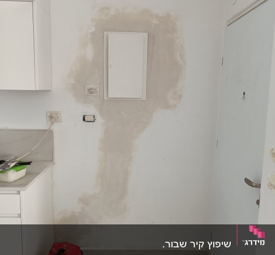 קיר עם תיקוני טיח, כלי עבודה אדום על הרצפה